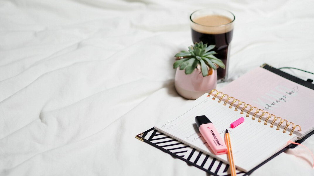 Mesa de trabalho organizada com caderno de anotações, planta e xícara de café