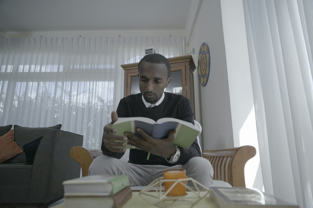 Homem brasileiro sentado lendo um livro em um sofá em casa
