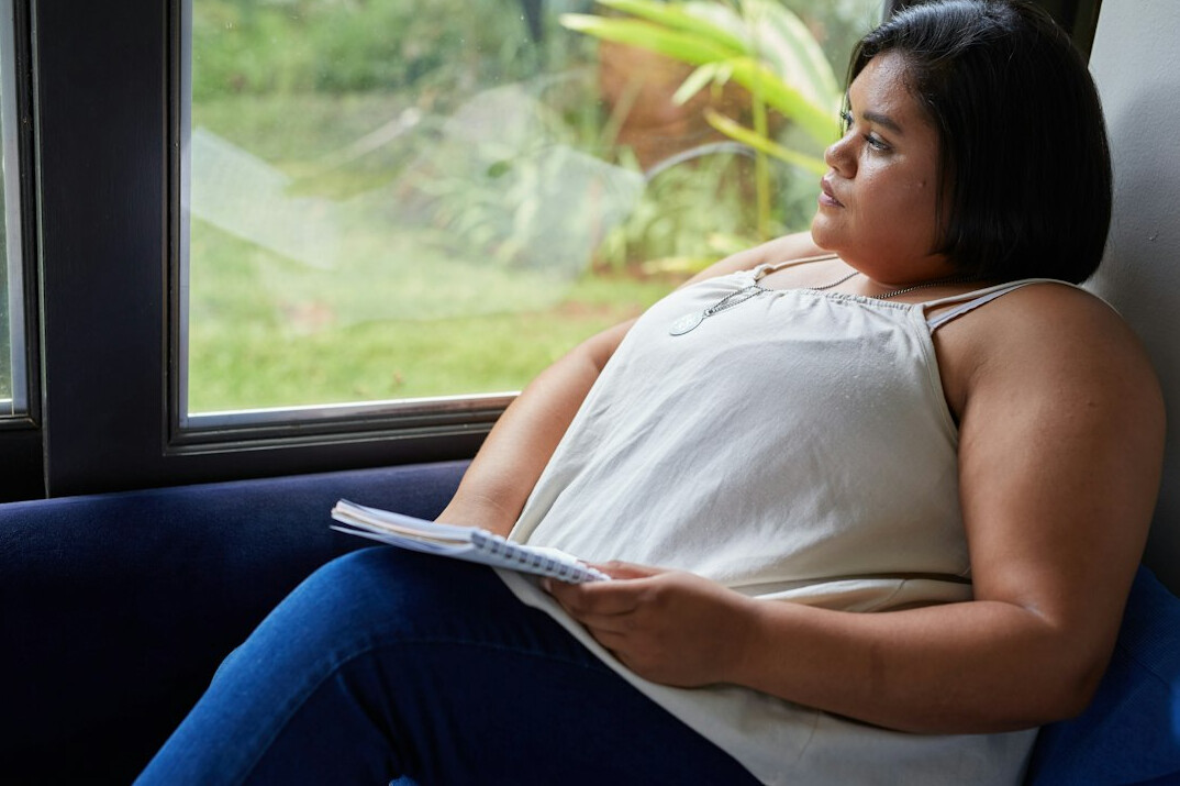 Jovem mulher brasileira escrevendo em um caderno junto a uma janela